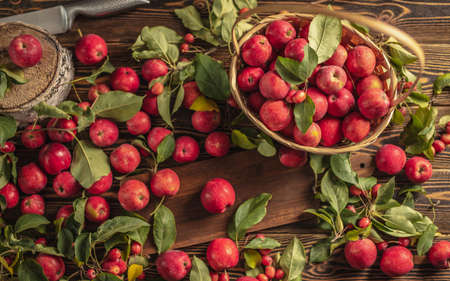 Appetizing red apples with green leaves on a wooden table and in a basket. Fresh harvest and autumn mood.の写真素材