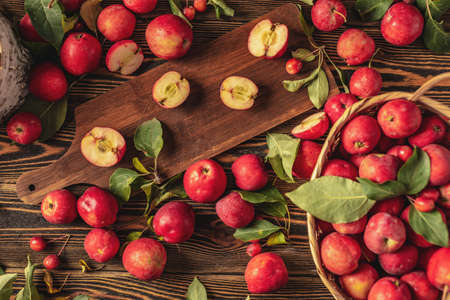 Appetizing organic red apples with green leaves on a wooden table and in a basket. Fresh harvest and autumn mood. top viewの写真素材