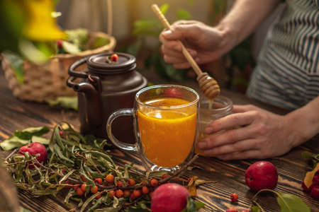 Woman is making a tasty and healthy vitamin tea from fresh sea buckthorn berries with honey. Concept of a cozy autumn atmosphere and health care during colds and flu season.の写真素材