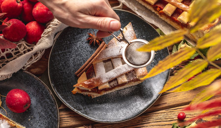 Hand of person is sprinkling a piece of homemade apple pie with powdered sugar. Concept of a cozy autumn atmosphere with the smell of fresh pastries.の写真素材