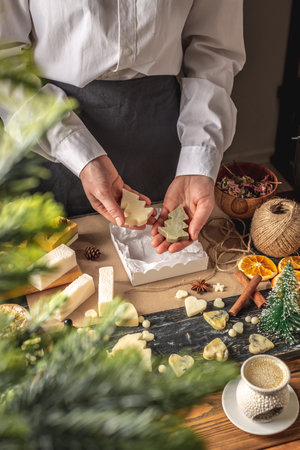 Woman is packing handmade soap in the shape of Christmas trees into a gift box. Concept of preparing for the New Year holidays, choose presents, useful eco friendly natural gifts.の写真素材