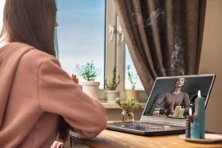 Woman is sitting at a table in front of a laptop, meditating and relaxing while listening to an instructor online on the video session. Concept of a remote therapy and meditation with a coach.の写真素材