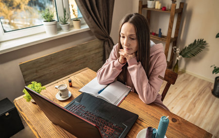 Woman is sitting in front of a computer screen in a calm pleasant atmosphere and attentively listens to video training or distance lesson.の写真素材