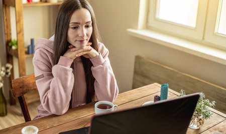 Woman is sitting in front of a computer screen in a calm pleasant atmosphere and attentively listens to video training or attends an online session with a mentor or just communicates with a friend.の写真素材