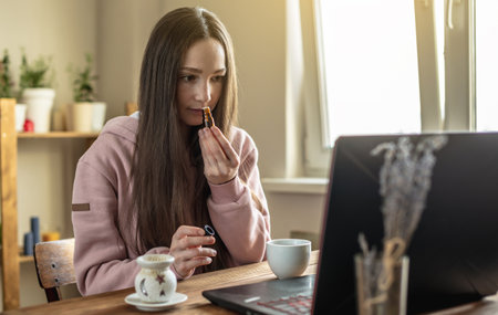 Woman sits in front of a computer screen and sniffs essential oil from a bottle to relax and restore energy or for distance learning on oils and meditation session.の写真素材