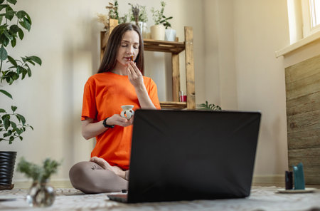 Woman is sitting on the floor in front of a laptop in a lotus position and sniffing the aroma oil. Concept of remote meditation, yoga and aromatherapy.の写真素材