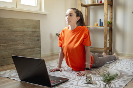 Woman in a bright clothes on the floor in front of a laptop is doing yoga using a video lesson.の写真素材