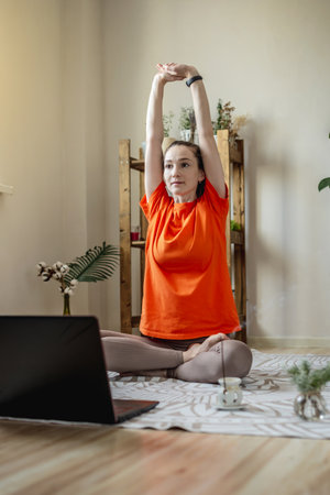 Woman in a bright clothes on the floor in front of a laptop is doing yoga using a video lesson.の写真素材