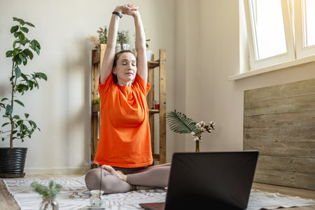 Woman in a bright clothes on the floor in front of a laptop is doing yoga using a video lesson.の写真素材