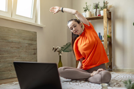 Woman in a bright clothes on the floor in front of a laptop is doing yoga using a video lesson.の写真素材
