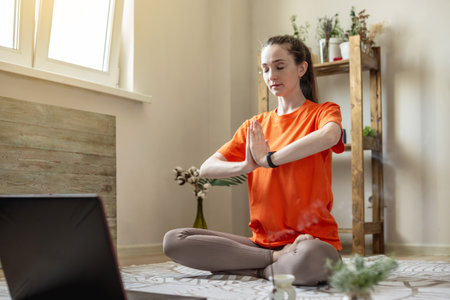 Woman in a bright clothes on the floor in front of a laptop is doing yoga using a video lesson.の写真素材