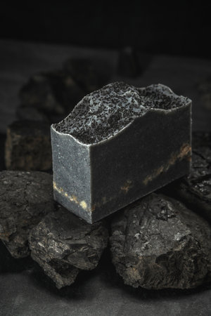 Natural charcoal soap on real coals on a black background. Concept of making and using organic eco soaps and cosmetics.の写真素材