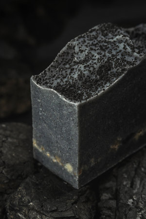 Natural charcoal soap on real coals on a black background. Concept of making and using organic eco soaps and cosmetics. vertical and closeupの写真素材