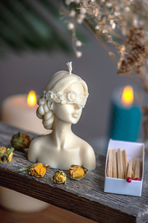 Beautiful feminine handmade candle in the shape of a female body on a wooden stand. There are matches and yellow rose buds nearby.の写真素材