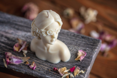Beautiful handmade candle in the shape of a female body on a wooden stand surrounded by flower petals.の写真素材