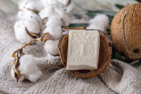 A piece of white soap with the inscription Natural and the image of a tree, coconut and cotton on the table.の写真素材
