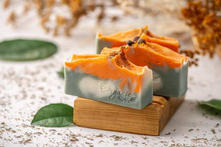 Pieces of bright natural handmade soap on a wooden soap dish with green leaves around.の写真素材
