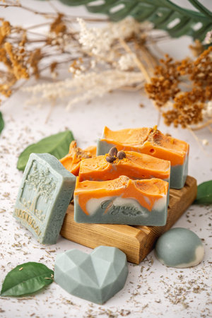Pieces of bright natural handmade soap on a wooden soap dish with green leaves around.の写真素材