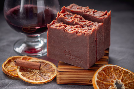 Pieces of handmade natural wine soap on a wooden soap dish, a glass of wine and pieces of orange on a gray background.の写真素材