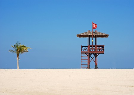 Red flag on the beach. A lifeguards hut ant palm tree.の写真素材
