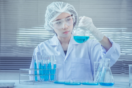 Female medical or research scientist or doctor using looking at a test tube of clear solution in a lab or laboratoryの写真素材