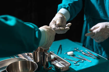 Two surgeons working in operating room, one hand over surgical equipment to another. Surgeons hands...