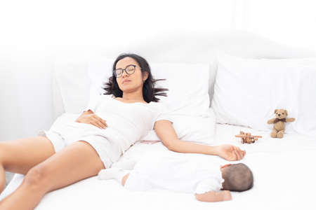 Tired mother laid in bed with newborn baby at night.の写真素材