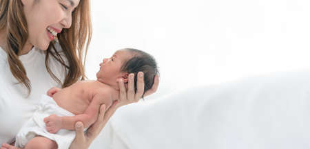 Close up portrait of beautiful young asian mother with newborn baby. Side view of a young woman playing with her little baby.の写真素材