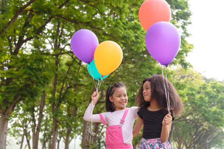 Cute african american and Asian little girl playing outdoor. Friends happy playing with holding a colorful balloon.の写真素材