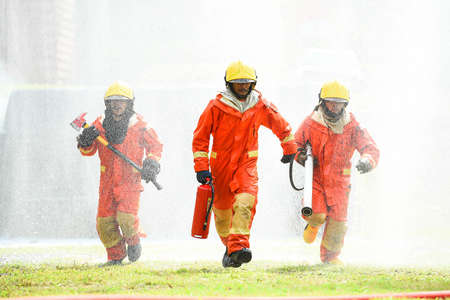 Three firefighters in uniform walking forward holding a fire extinguish tools surround with water...