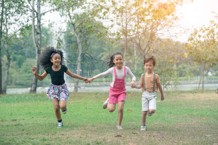 Group of young children happily  holding hands and running towards camera in park.の写真素材