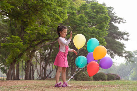 Little lovely girl holding a colorful ballons smiling in the park. Girls has a happy holiday.の写真素材