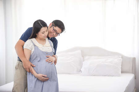 Asian couple sitting and embracing wife 8 months tummy.  Family waiting for newborn baby.の写真素材