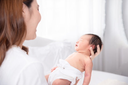 Asian loving mom carying of her newborn baby at home. Happy mum holding sleeping infant child on hands. Mother hugging her little one months old son.の写真素材