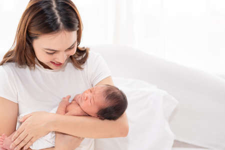 Asian loving mom carying of her newborn baby at home. Happy mum holding sleeping infant child on hands. Mother hugging her little one months old son.の写真素材