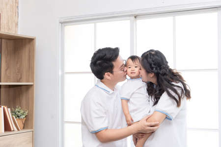 Asian happy family, father and mother kissing their baby at home.の写真素材
