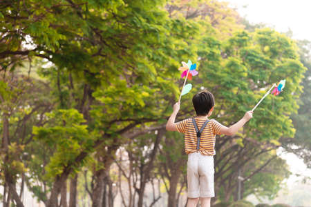 Boy playing with windmill, running, jumping in the park on summer vacation concept for freedom or the environmentの写真素材
