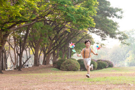Boy playing with windmill, running, jumping in the park on summer vacation concept for freedom or the environmentの写真素材