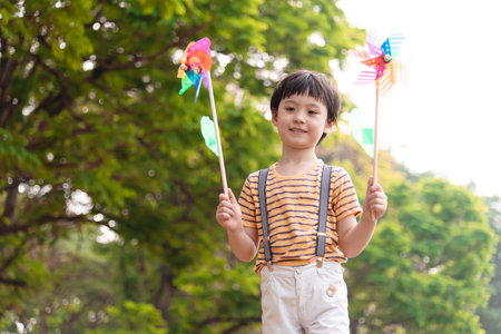 Boy playing with windmill, running, jumping in the park on summer vacation concept for freedom or the environmentの写真素材