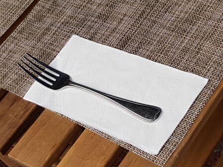 Spoon and knife on napery, table cloth mat on wood dining table in restaurant of hotel.の写真素材