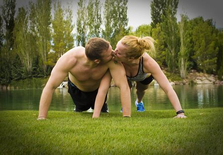 A man and woman holding the plank position of a pushup while kissing each other.の写真素材