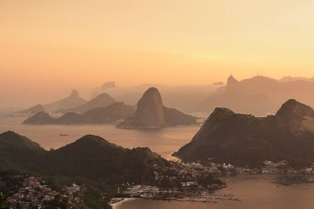 Orange sunset view from the mountains of the "City Park" in Niteroi, overlooking the dramatic peaks of Rio de Janeiro, Brazil, such as Sugarloaf and the Two Brothers.の写真素材