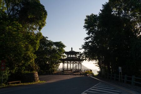 A clear blue sky sunrise over the Vista Chinesa Rotunda lookout in the Tijuca Forest mountains of Rio de Janeiro, Brazil. The shelter is silhouetted and viewed from the road surrounded by trees.の写真素材