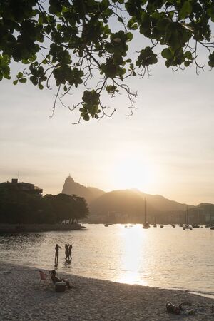 Rio de Janeiro, Brazil - March 26, 2019: Sunset from Praia da Urca Beach in Rio de Janeiro. People relax in the sand as the sun sets over the mountains and Christ the Redeemer Statue on Corcovado.のeditorial素材