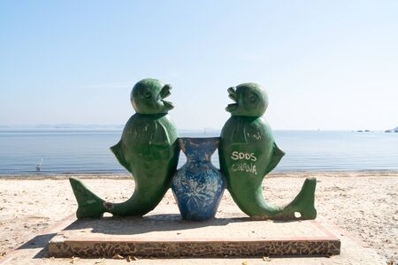 Rio de Janeiro, Brazil - July 25, 2019: An old painted decaying statue on the white sand at the beach on Ilha de Paqueta Island. There are two green fish facing each other with a blue vase between.のeditorial素材
