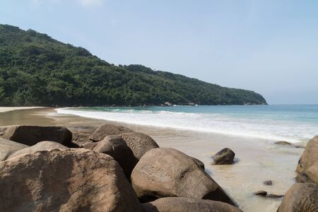 Early morning at the deserted Praia Lopes Mendes on Ilha Grande Island in the state of Rio de Janeiro, Brazil. There is blue sky, white sand, small waves, palm trees, mountains beyond, with no people.の写真素材