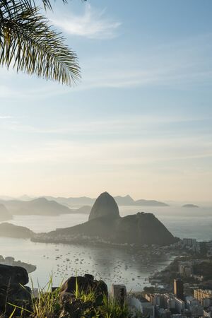 Sunrise view over Sugarloaf Mountain and Guanabara Bay from Mirante Dona Marta in Rio de Janeiro. The early morning golden light shines over the sea and the buildings of the Botafogo suburb and treesの写真素材