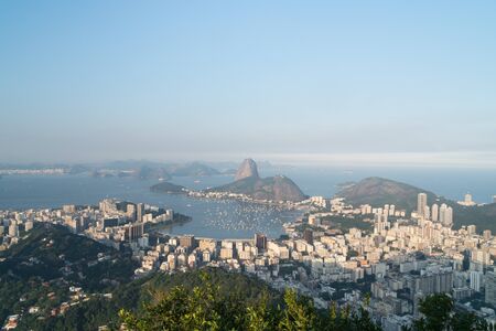 View over Sugarloaf Mountain, Botafogo suburb and Guanabara Bay from Mirante Dona Marta lookout, Rio de Janeiro on a clear evening with blue sky. The hill casts a shadow on the tall apartment buidingsの写真素材