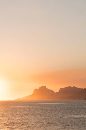 A golden sunset with orange clouds and blue sky over Pedra da Gavea and the mountains of the Tijuca Forest in Rio de Janeiro from Piratininga Beach in Niteroi, the city across the Guanabara Bay.の写真素材