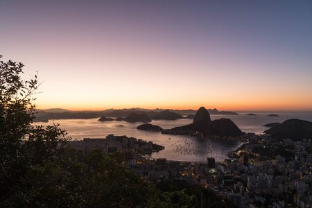 Sunrise from Mirante Dona Marta in Rio de Janeiro overlooking Sugarloaf Moutain, the suburb of Botafogo Guanabara Bay and Niteroi in the distance. There is orange light and a clear sky at dawn.の写真素材